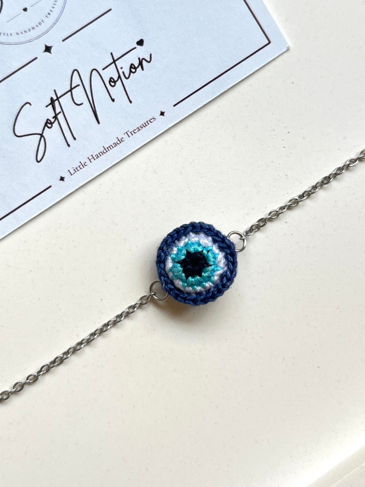 Close-up of miniature 3D crochet evil eye charm in navy blue, turquoise and white