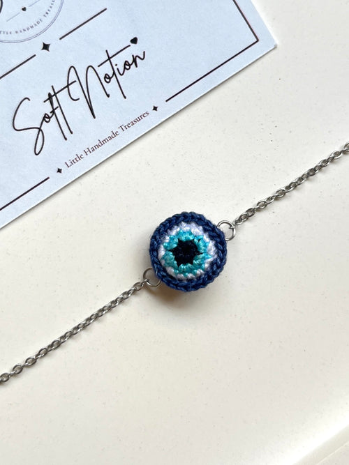 Close-up of miniature 3D crochet evil eye charm in navy blue, turquoise and white
