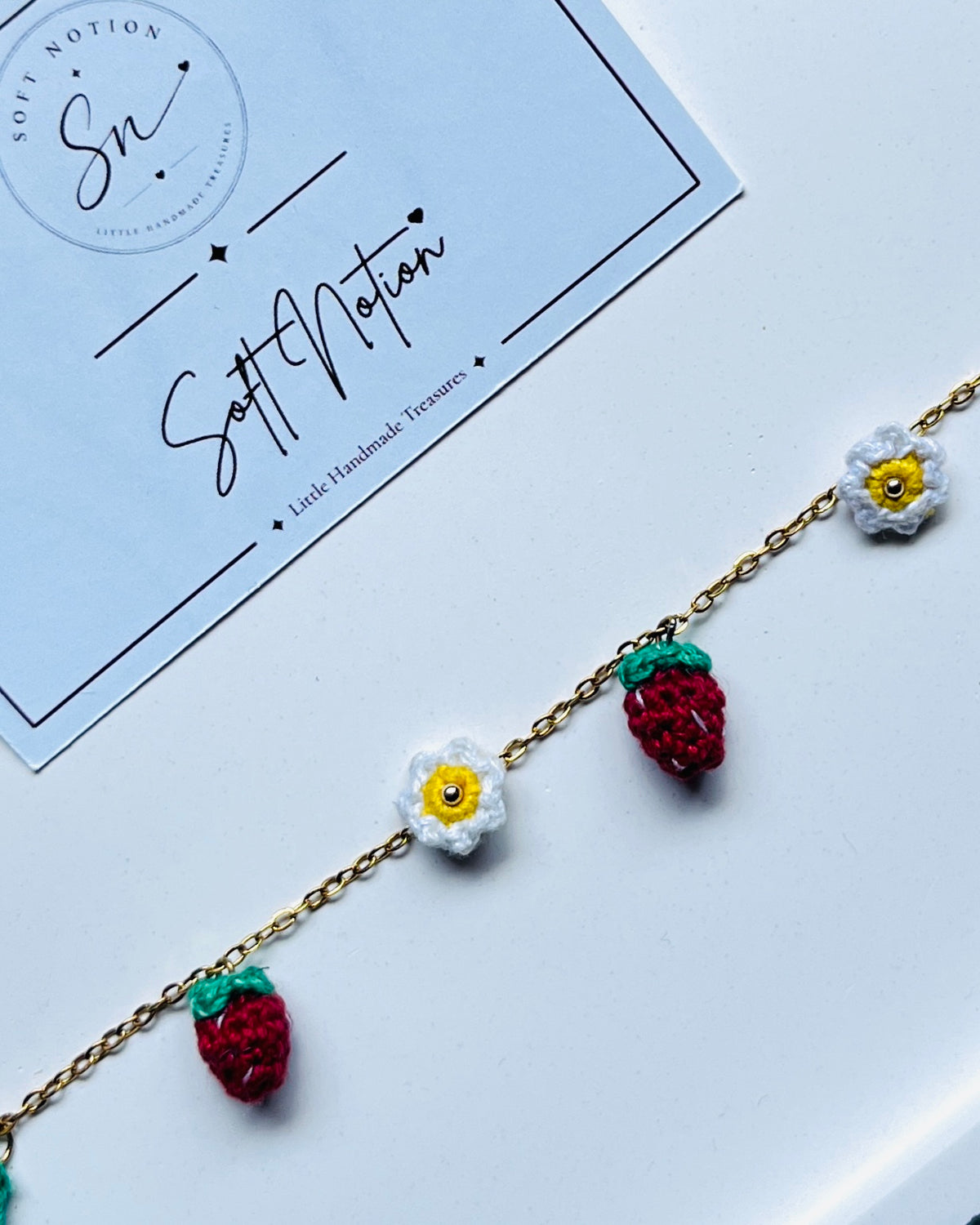 Close-up of hand-crocheted strawberry and daisy charms on the Strawberry Muse Bracelet