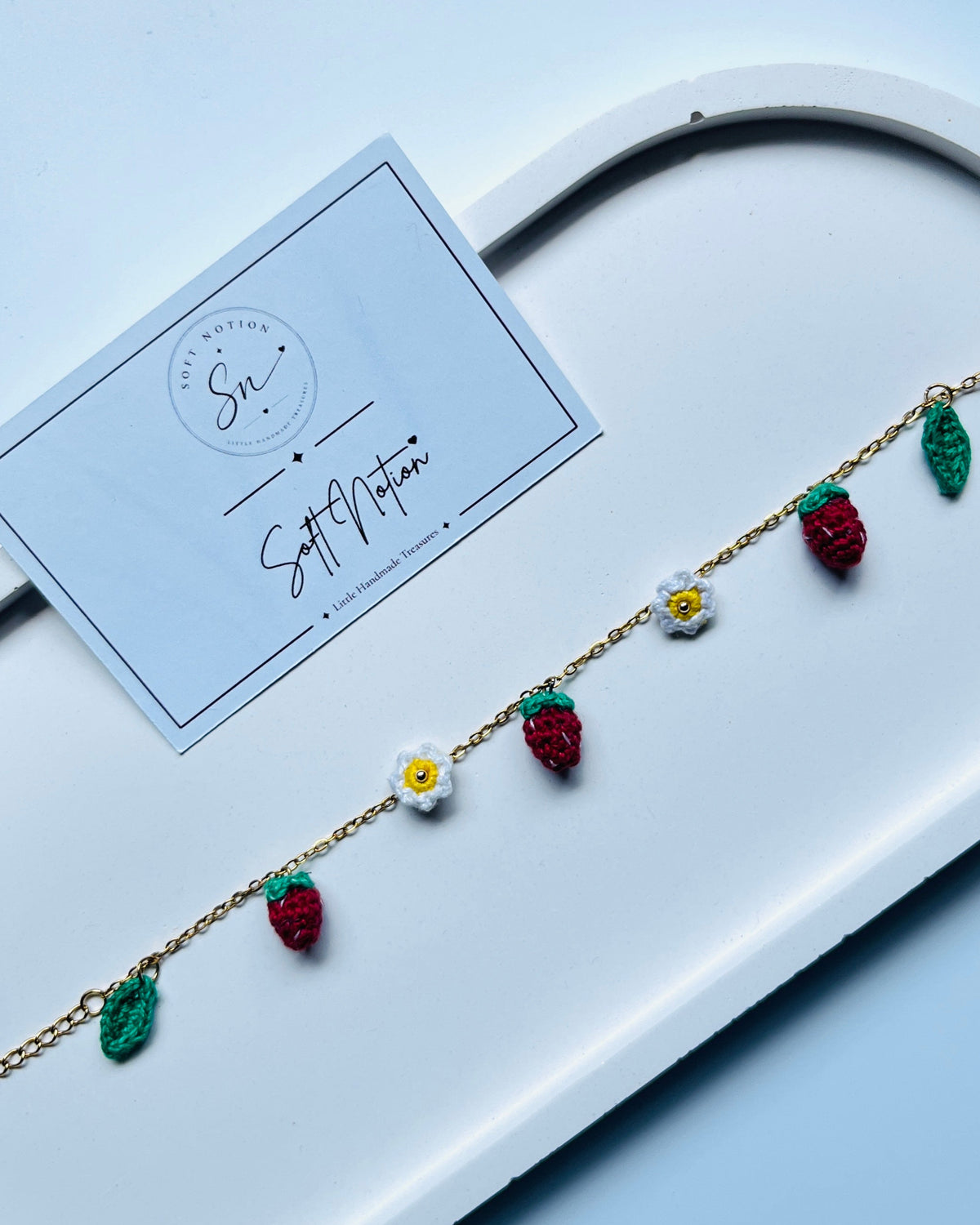 Strawberry Muse Bracelet with hand-crocheted strawberries, daisies and leaves on a gold-toned chain